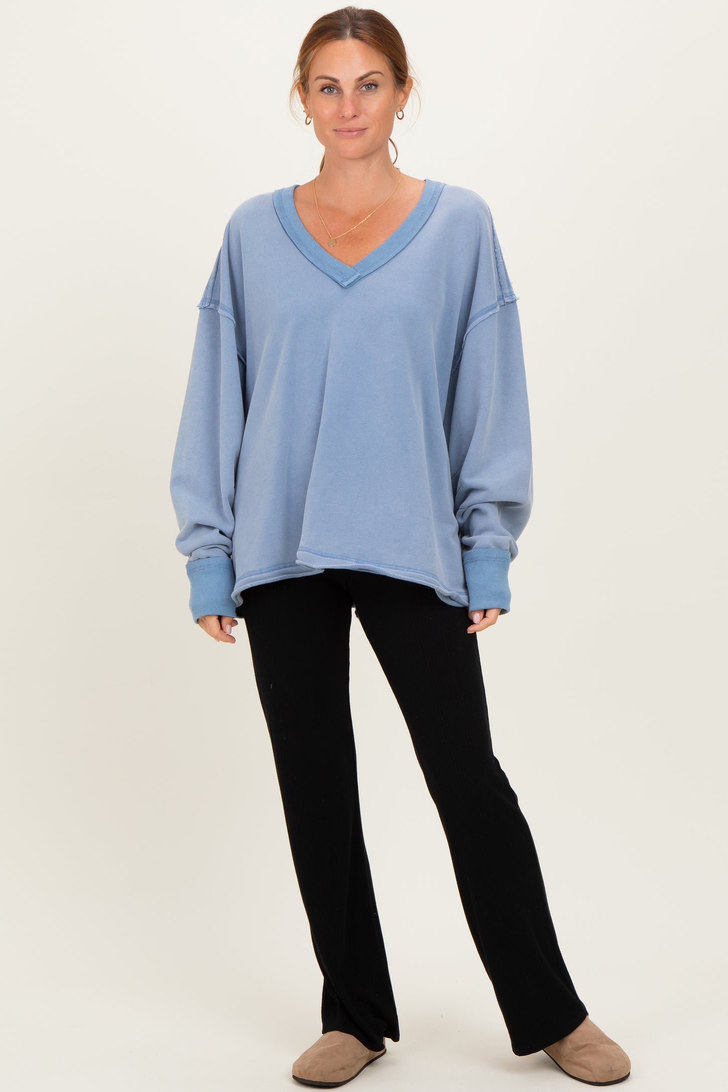 woman wearing a light blue oversized v-neck sweatshirt with black flared pants and beige slippers