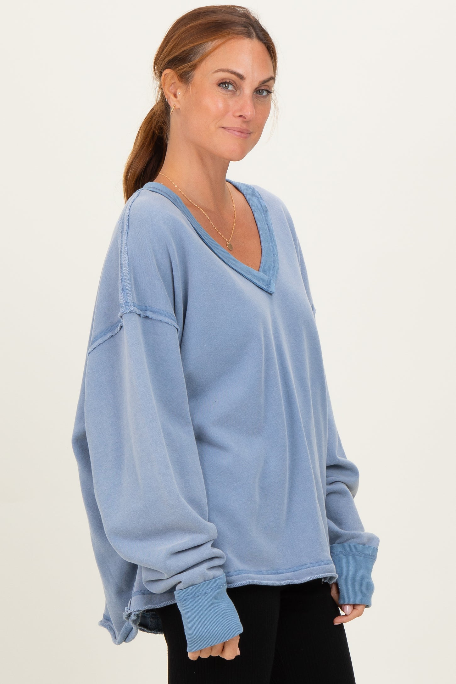 woman wearing a soft blue oversized v-neck sweatshirt with rolled sleeves and a relaxed fit