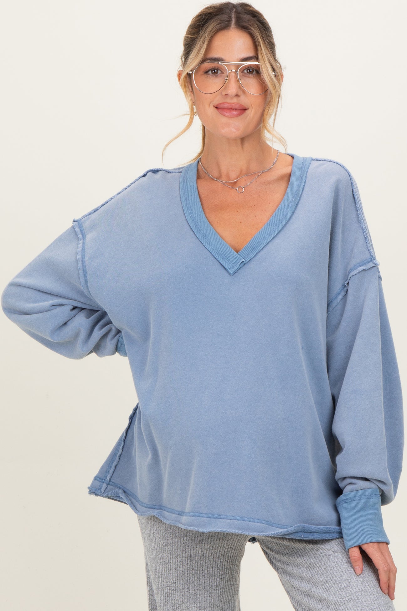 woman wearing a blue oversized v-neck maternity sweatshirt with stitching details and relaxed sleeves