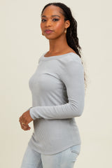 woman wearing a light grey ribbed long sleeve top and blue jeans, posing sideways with a gentle smile