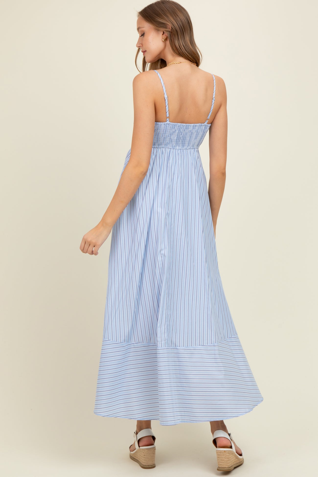 woman wearing a light blue striped maternity maxi dress with a smocked back and adjustable straps
