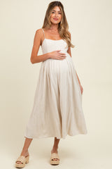woman wearing a light beige maternity dress with spaghetti straps and a flowy silhouette, holding her baby bump