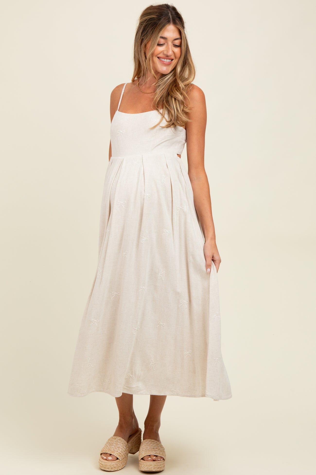 woman wearing a beige maternity dress with spaghetti straps and a flowing skirt, showing her baby bump