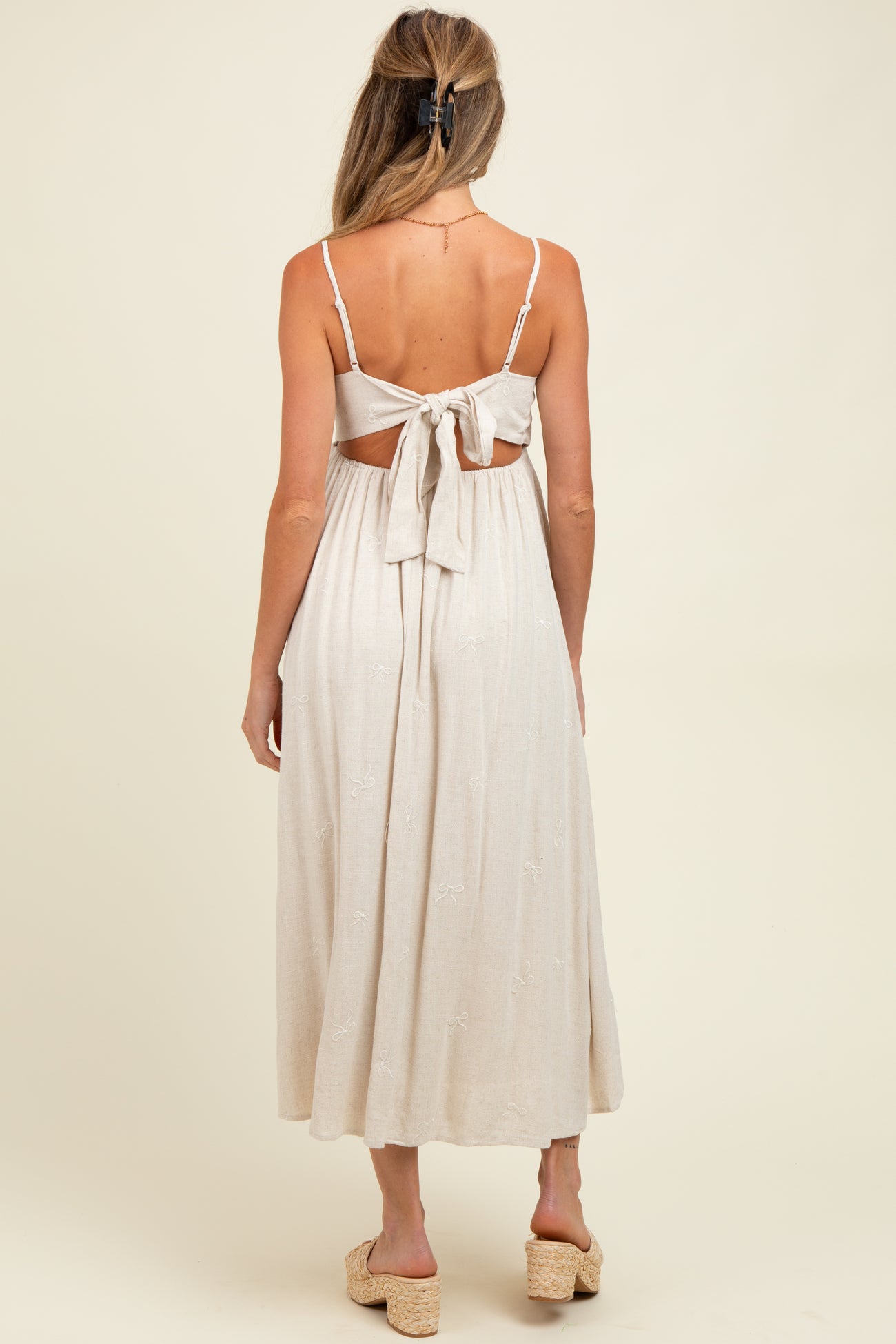 woman wearing a light beige maternity maxi dress with a tie-back detail and delicate embroidery