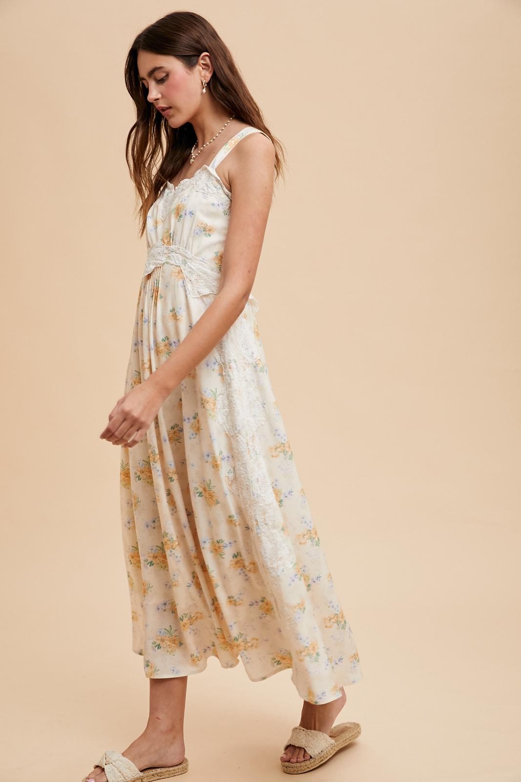 woman wearing a floral print maxi dress with lace detailing and braided straps, styled with casual footwear