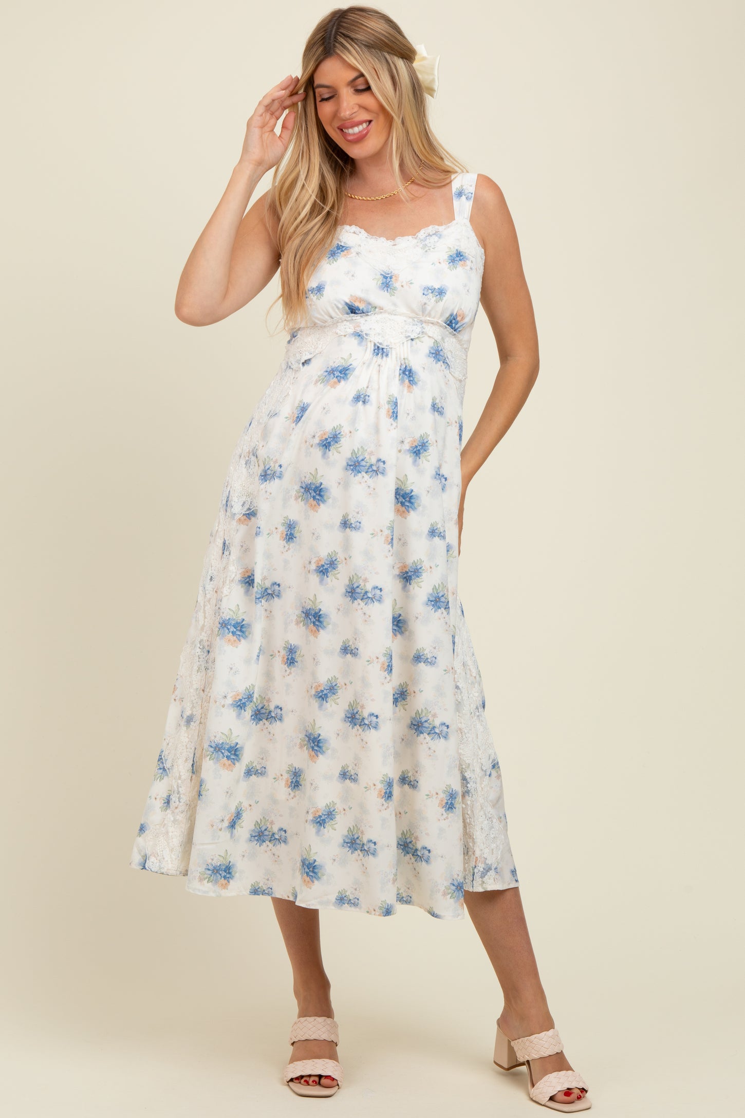 woman wearing a floral print white maternity dress with blue accents, featuring adjustable straps and a flowing skirt