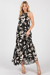 woman wearing a black and cream floral maxi dress with a halter neckline and flowy skirt, posing with one hand in pocket