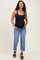 woman wearing a black maternity tank top and blue cropped jeans, showing her baby bump while smiling