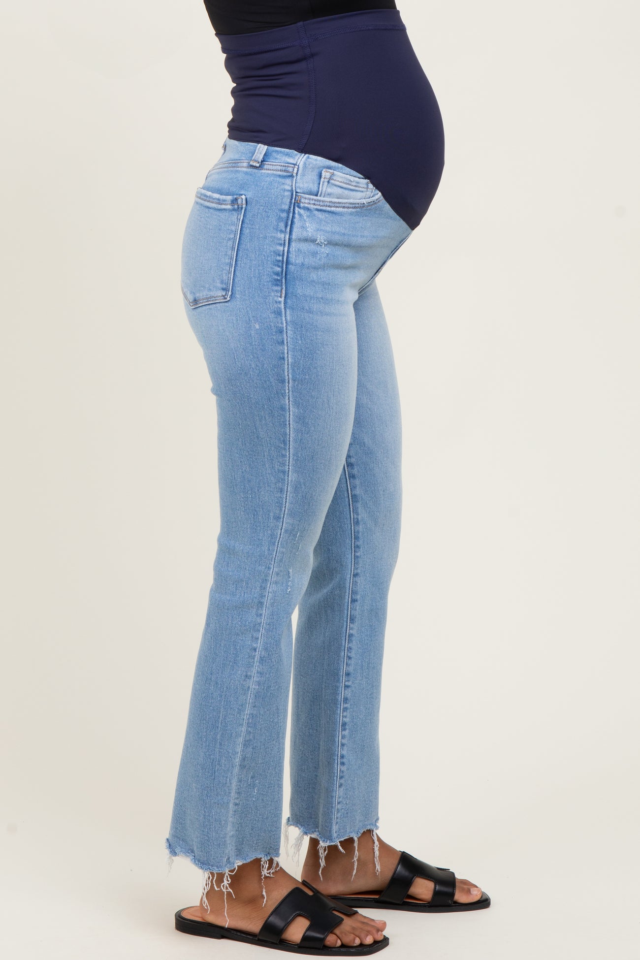 woman wearing light blue distressed maternity jeans with a visible baby bump