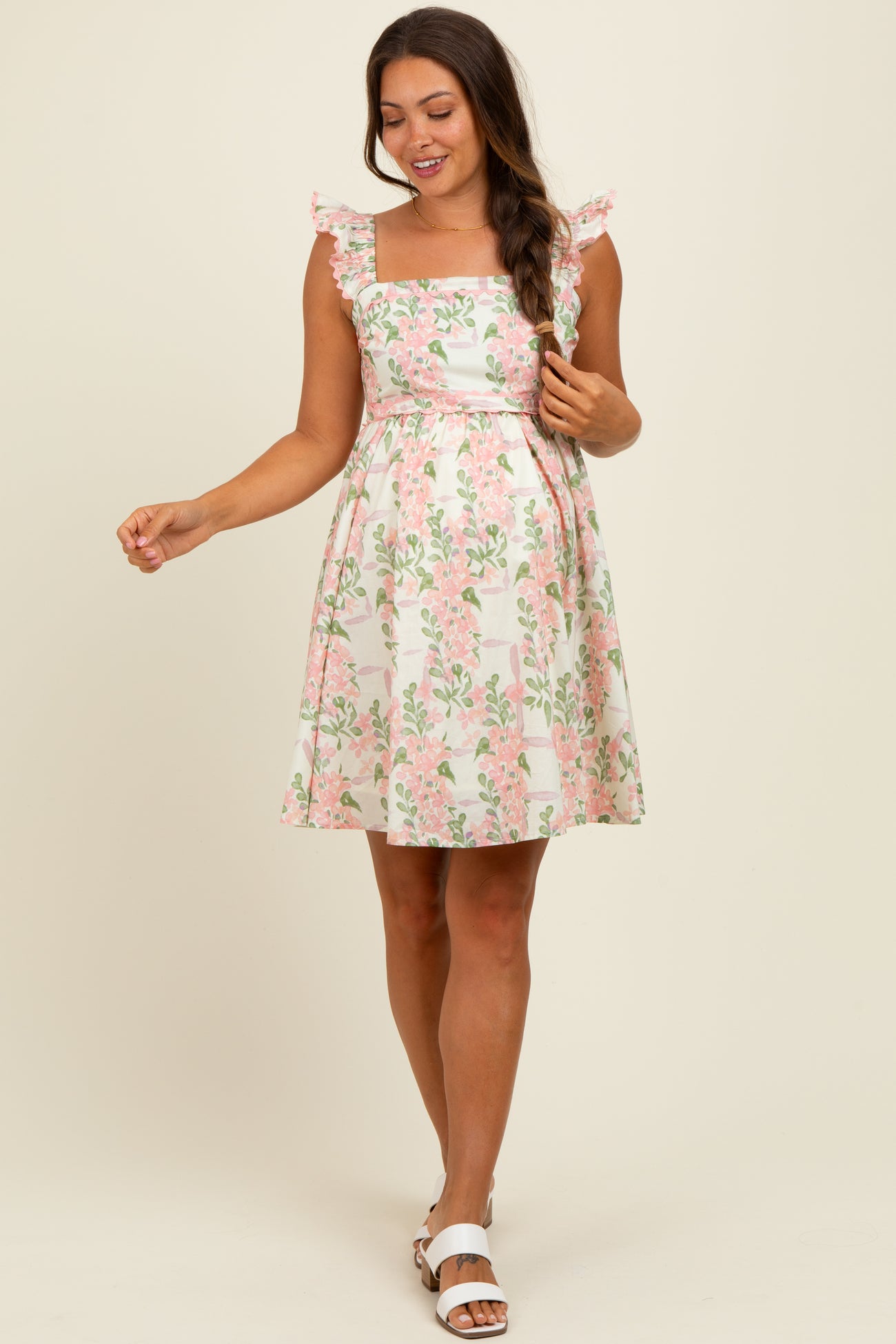 woman wearing a white floral maternity dress with ruffled straps and a fitted bodice, holding her baby bump