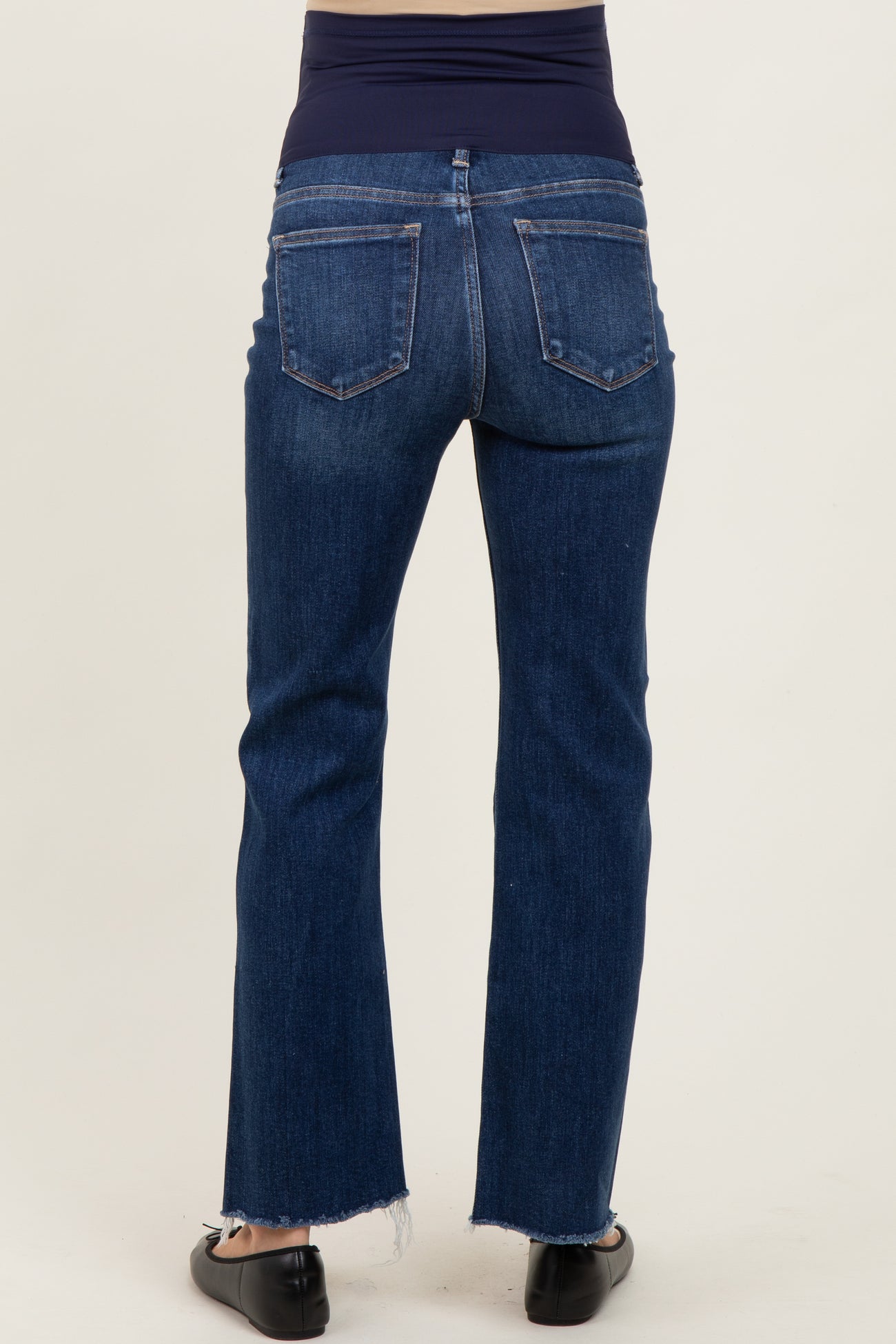 woman wearing dark blue maternity jeans with a stretchy waistband, showing the back view and frayed hem detail