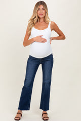 woman wearing a white maternity tank top and blue flared jeans, gently holding her baby bump