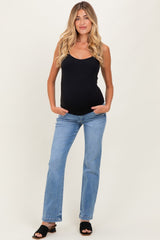 woman wearing a black maternity tank top and light blue maternity jeans, hands in pockets, with a visible baby bump
