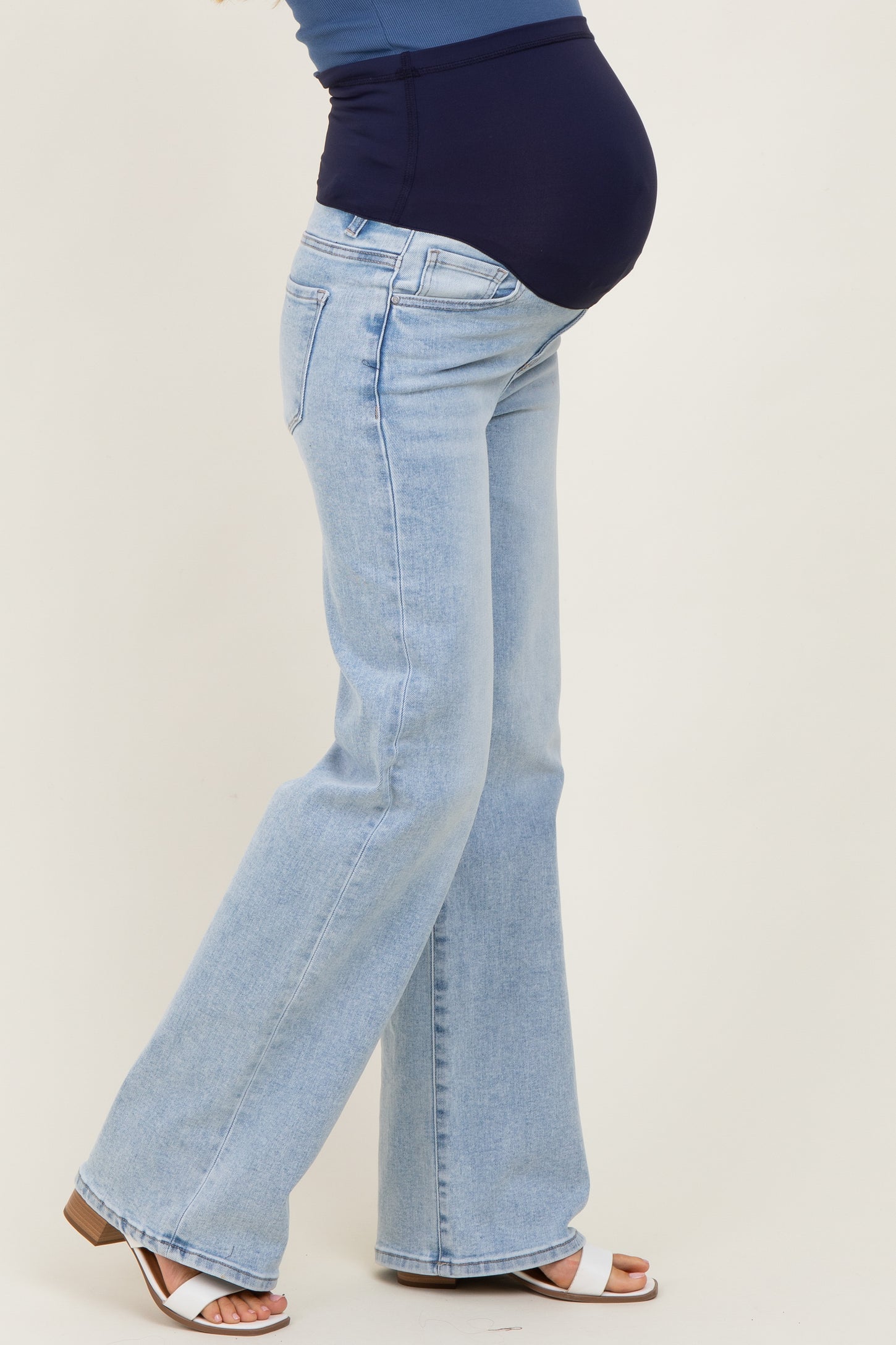 woman wearing light blue maternity flare jeans with a dark blue over-the-bump waistband and visible baby bump