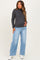 woman wearing a dark gray maternity turtleneck sweater and light blue wide-leg jeans, with a visible baby bump