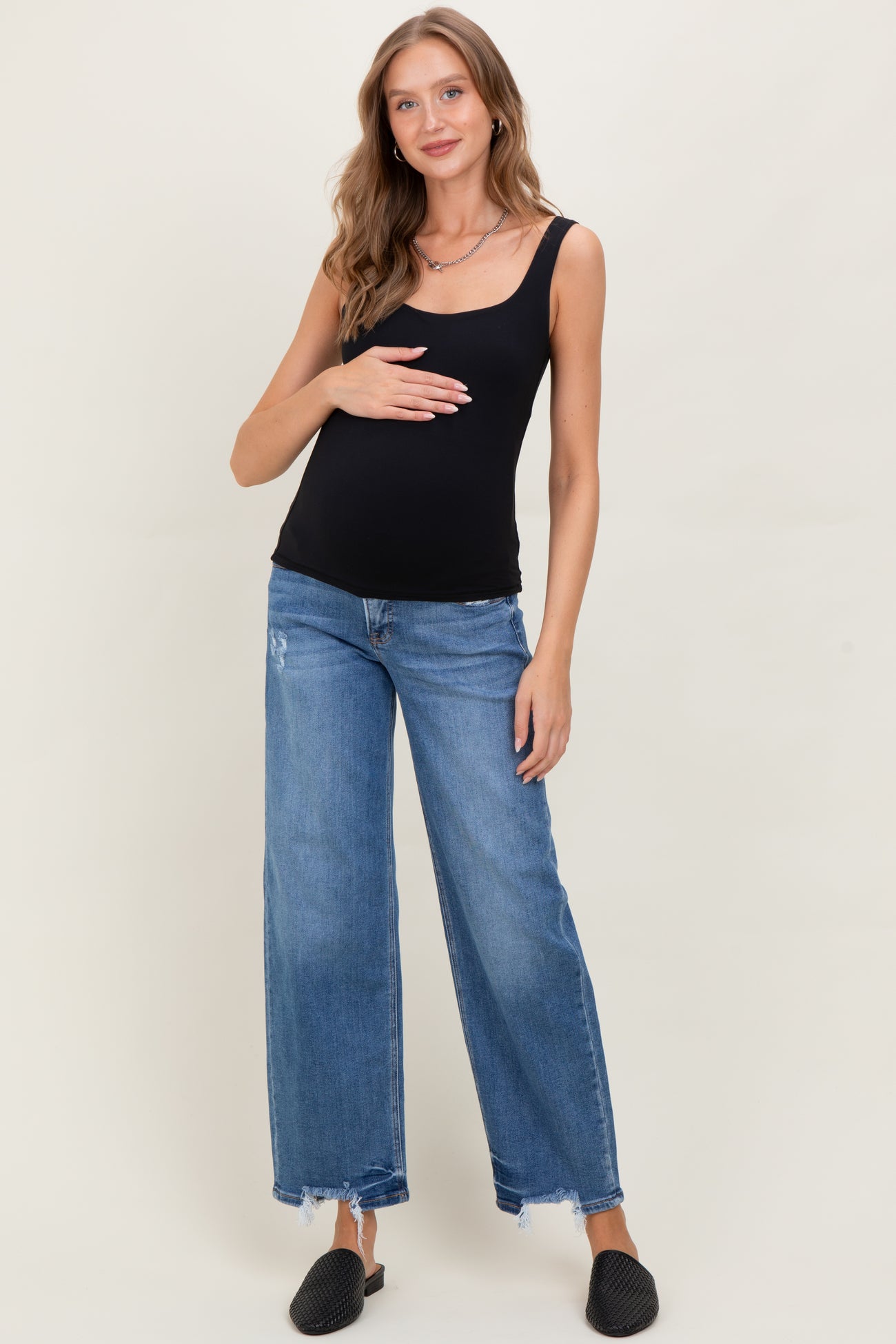 woman wearing a black maternity tank top and light blue wide-leg jeans, gently cradling her baby bump