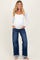 woman wearing a white long sleeve maternity top and high-waisted blue jeans, showing her baby bump