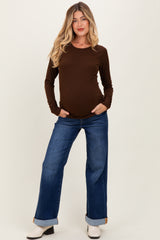 woman wearing a brown long sleeve maternity top and blue wide-leg jeans, showcasing a visible baby bump