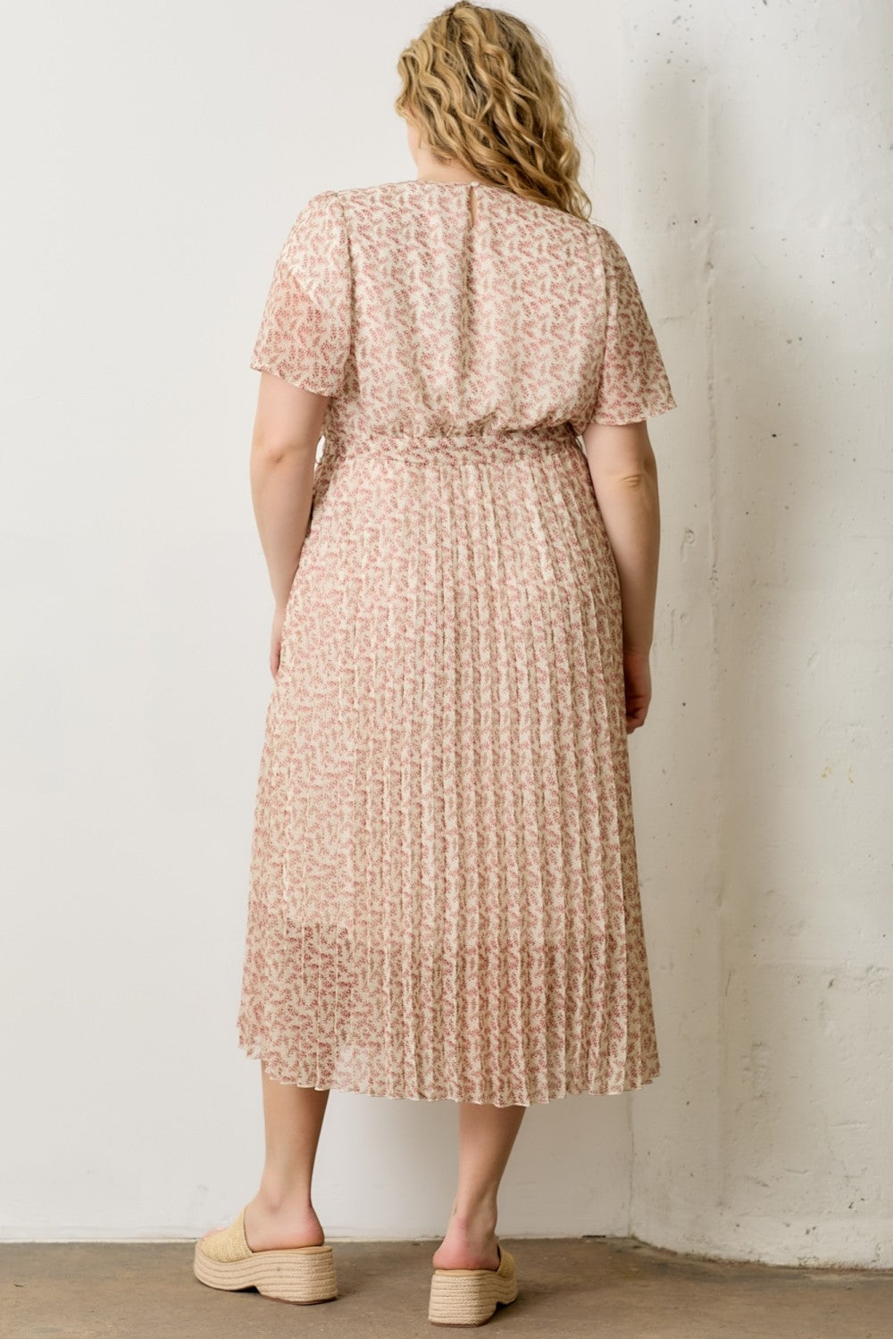 woman wearing a pink floral print plus-size midi dress with short sleeves and a pleated skirt viewed from the back