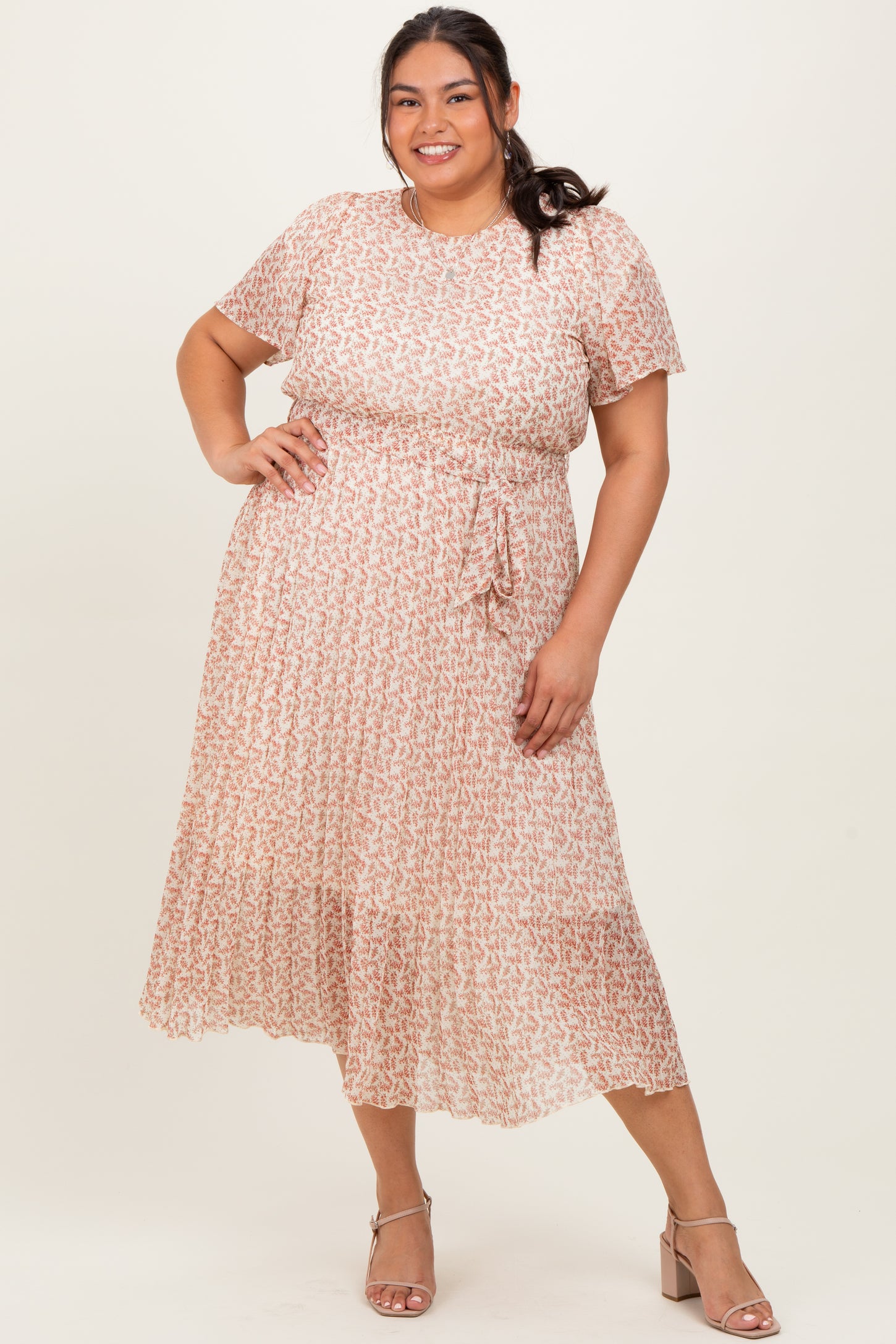 woman wearing a pink and white patterned plus size midi dress with short sleeves and a tie waist detail