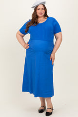 woman wearing a bright blue short sleeve maternity dress with a fitted bodice and a flowing skirt, displaying her baby bump