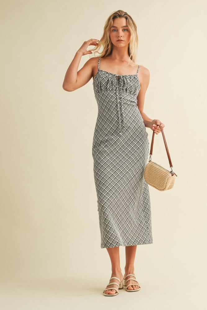 woman wearing a black and white patterned midi dress with spaghetti straps, holding a small woven bag
