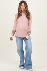 woman wearing a light pink ribbed maternity top with patterned sleeves and flared blue jeans, showcasing her baby bump