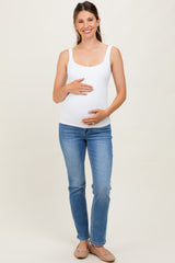 woman wearing a white maternity tank top and blue jeans, holding her baby bump with a smile