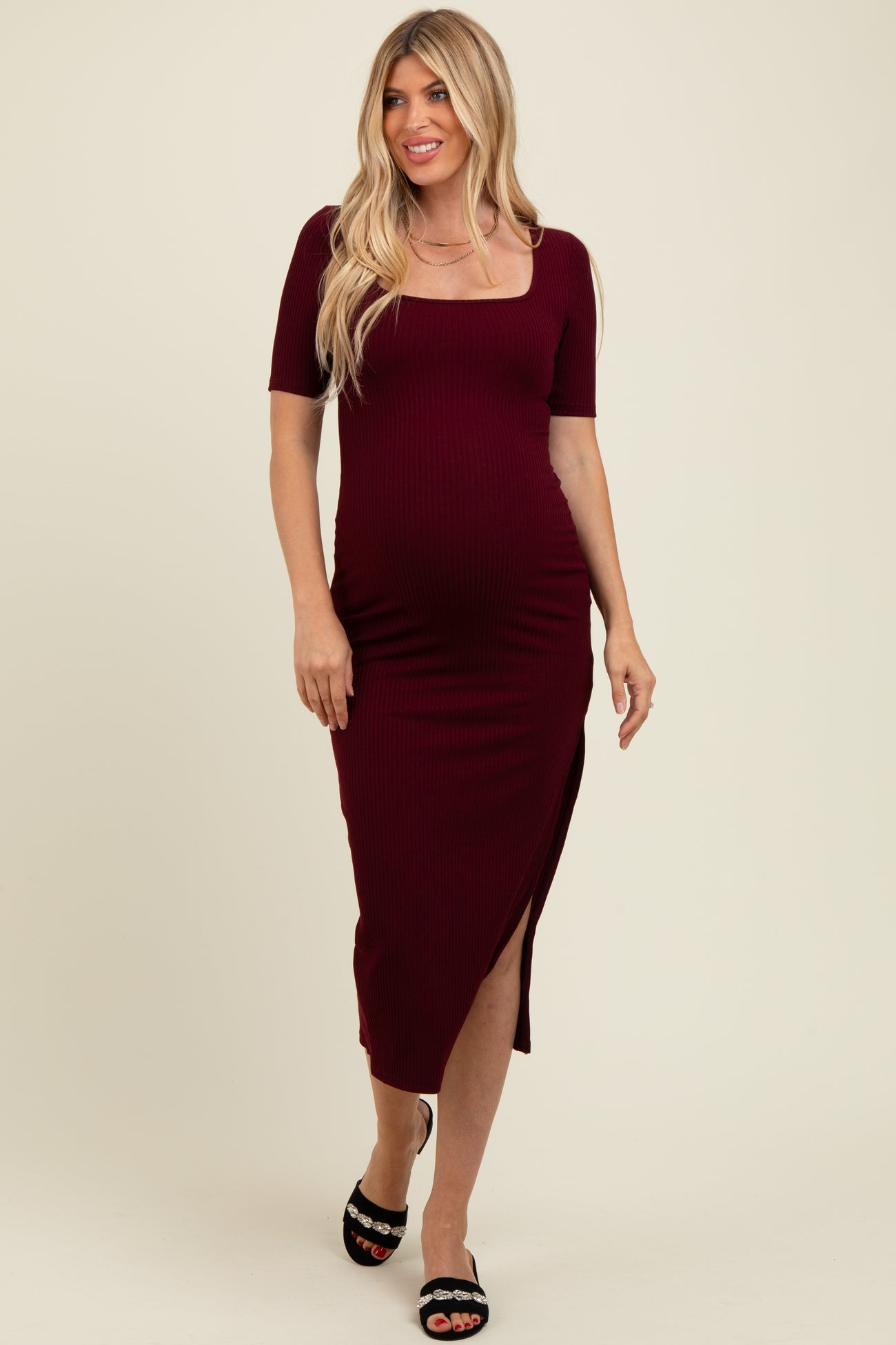 woman wearing a burgundy ribbed maternity dress with a square neckline and side slit, showing her baby bump