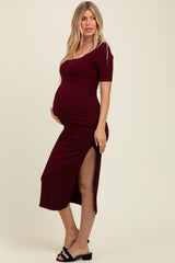 woman wearing a burgundy ribbed maternity dress with short sleeves and a thigh-high slit, showing her baby bump