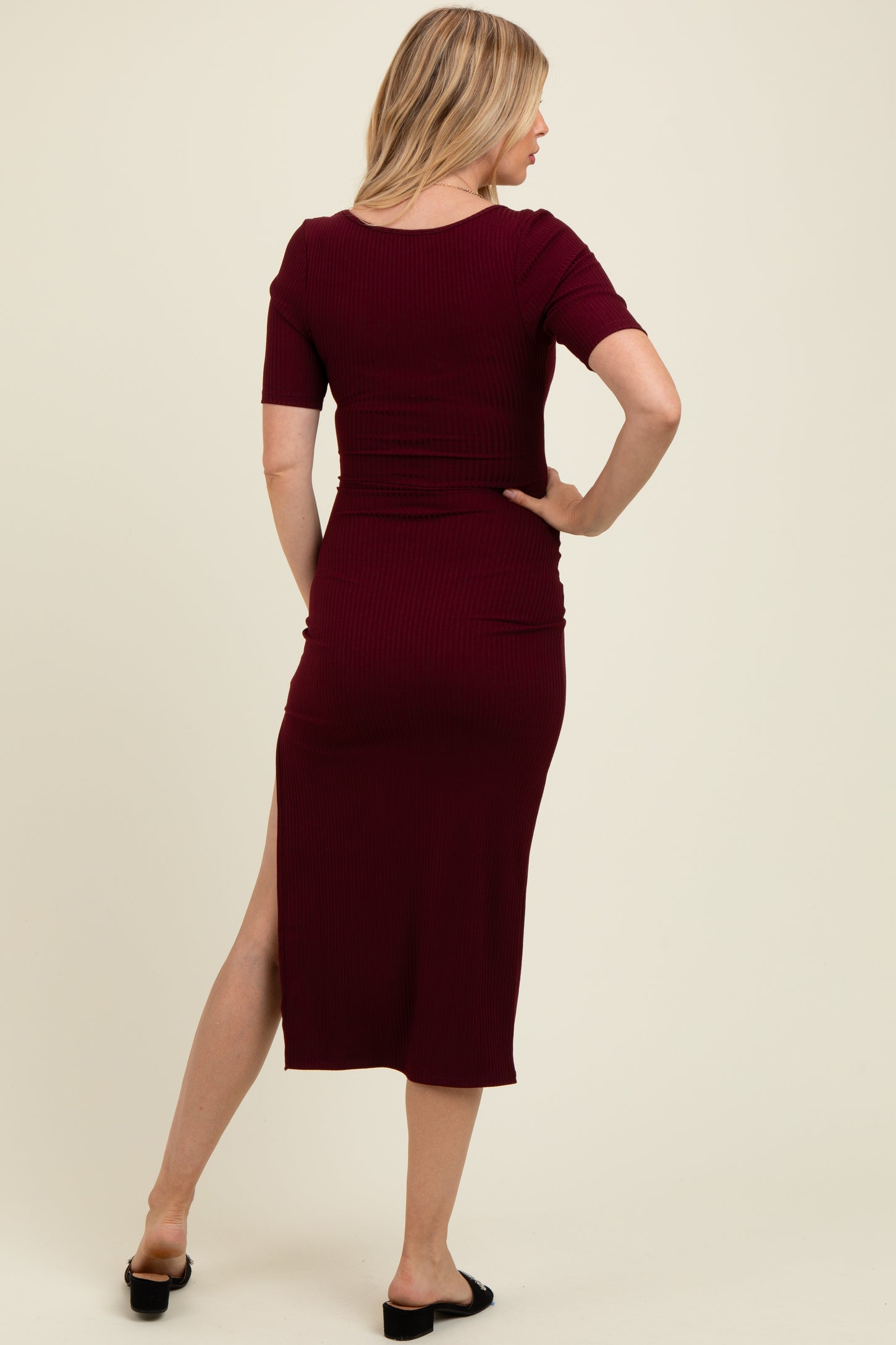 woman wearing a burgundy ribbed maternity dress with short sleeves and a side slit, showcasing her baby bump