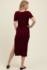 woman wearing a burgundy ribbed maternity dress with short sleeves and a side slit, showcasing her baby bump