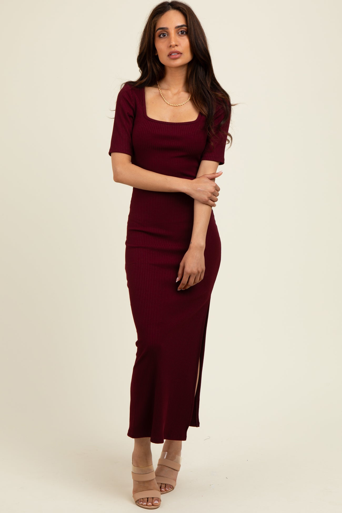 woman wearing a burgundy ribbed maxi dress with short sleeves and a side slit, styled with beige heels