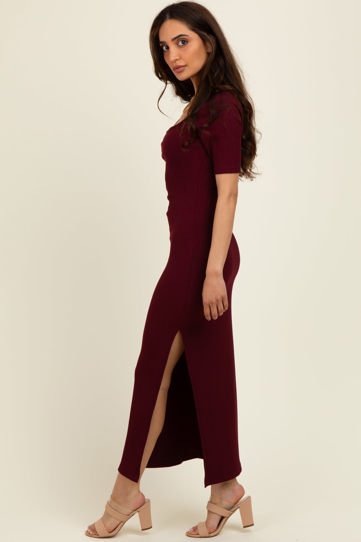 woman wearing a burgundy ribbed maxi dress with short sleeves and side slits, standing sideways in heels