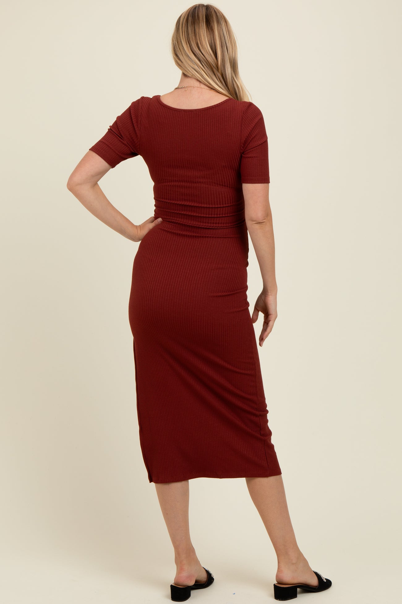 woman wearing a rust colored short sleeve ribbed maternity dress, view from the back