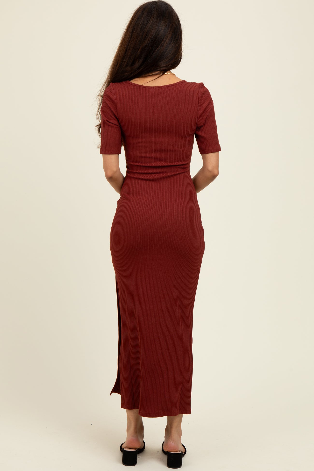woman wearing a rust-colored ribbed maxi dress with short sleeves and a side slit, seen from the back