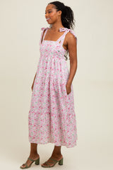 woman wearing a pink floral maxi dress with bow tie straps and pockets, standing sideways with a relaxed pose
