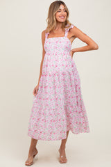 woman wearing a sleeveless pink floral maternity dress with tie straps and a tiered skirt, showcasing her baby bump