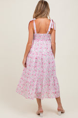woman wearing a pink floral maternity dress with adjustable straps and a flowy tiered skirt, showing her back and baby bump