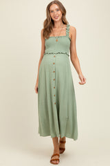 woman wearing a light green maternity maxi dress with a smocked bodice and button details, styled with a casual look