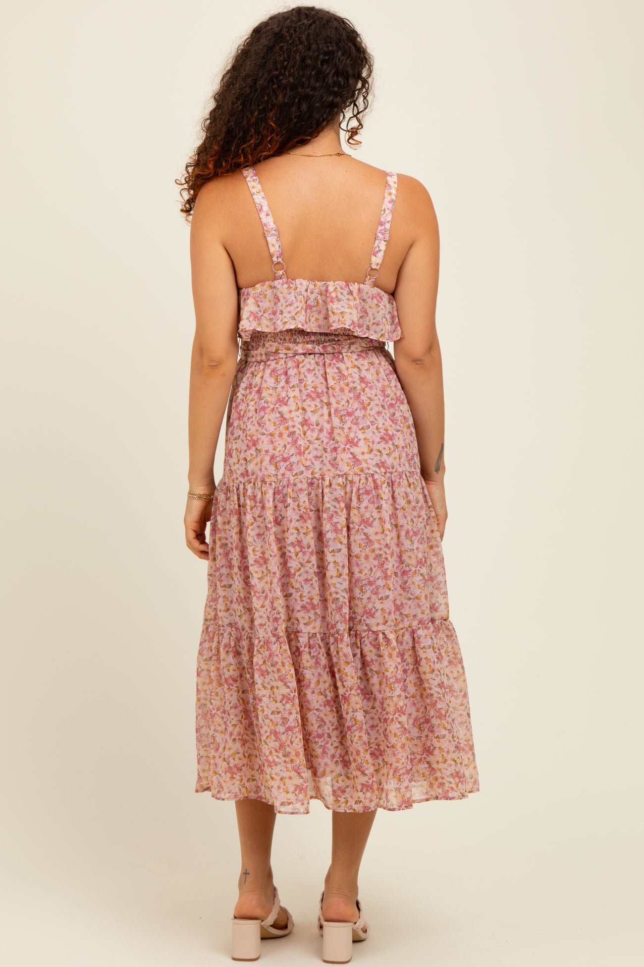 woman wearing a pink floral maternity dress with a ruffled top and tiered skirt, showing her back