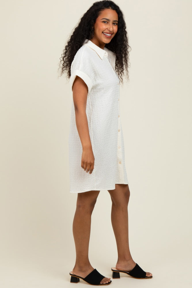 woman wearing a white short-sleeve button-down dress with a textured fabric and black slide sandals