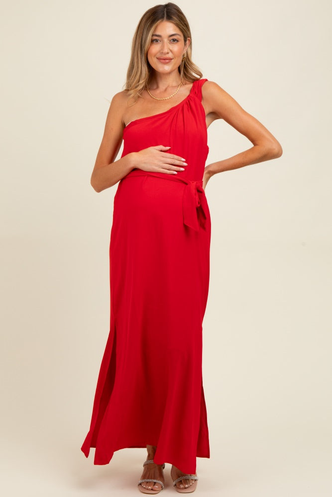 woman wearing a red one-shoulder maternity dress with a side tie and holding her baby bump