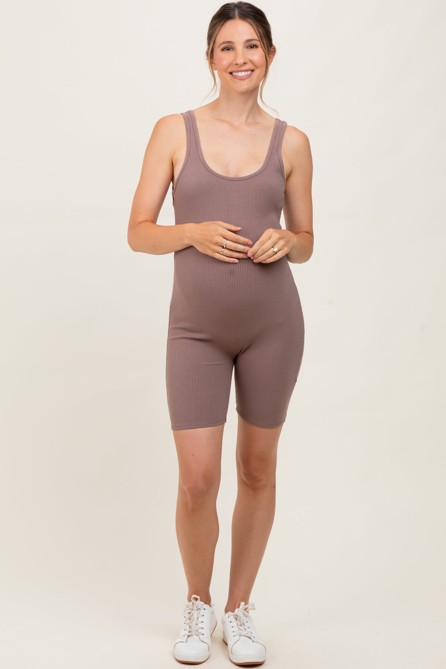woman wearing a mauve ribbed maternity romper with a visible baby bump and white sneakers
