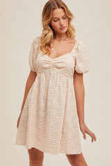 woman wearing a light pink checkered puff sleeve dress with a square neckline and a gathered waist