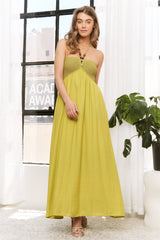 woman wearing a yellow maxi dress with a smocked bodice and a keyhole detail, standing in front of a large window