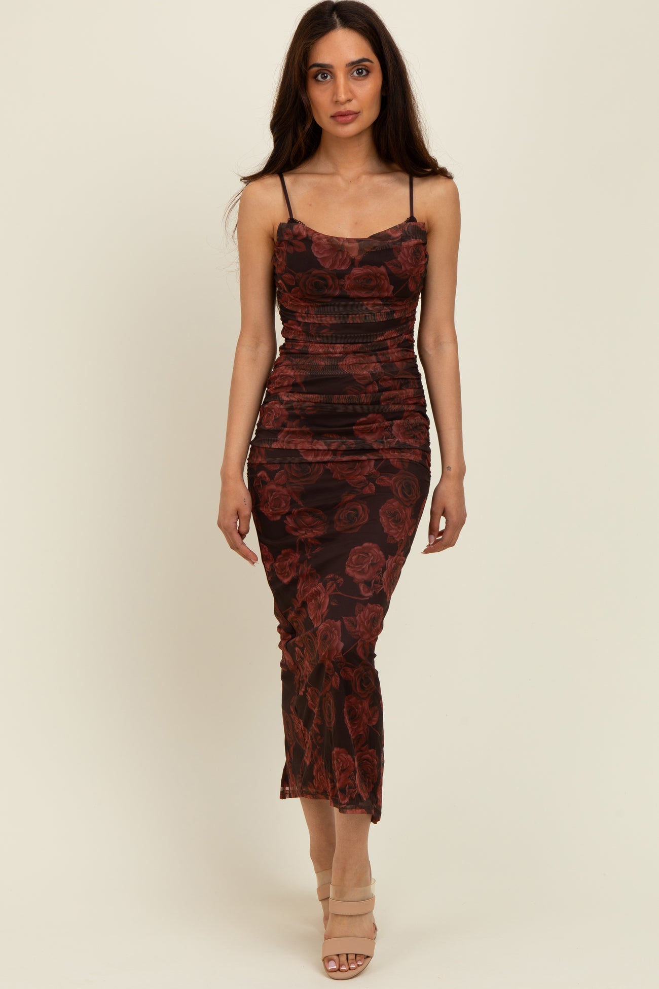 woman wearing a fitted black dress with red rose prints and thin straps, standing against a neutral background