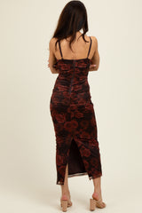 woman wearing a black floral ruched midi dress with a back zipper and a side slit, viewed from the back