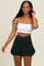 woman wearing a white crop top and a dark green skater skirt, smiling and touching her hair