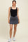 woman wearing a black maternity tank swimsuit with a grey skirt overlay and white sneakers